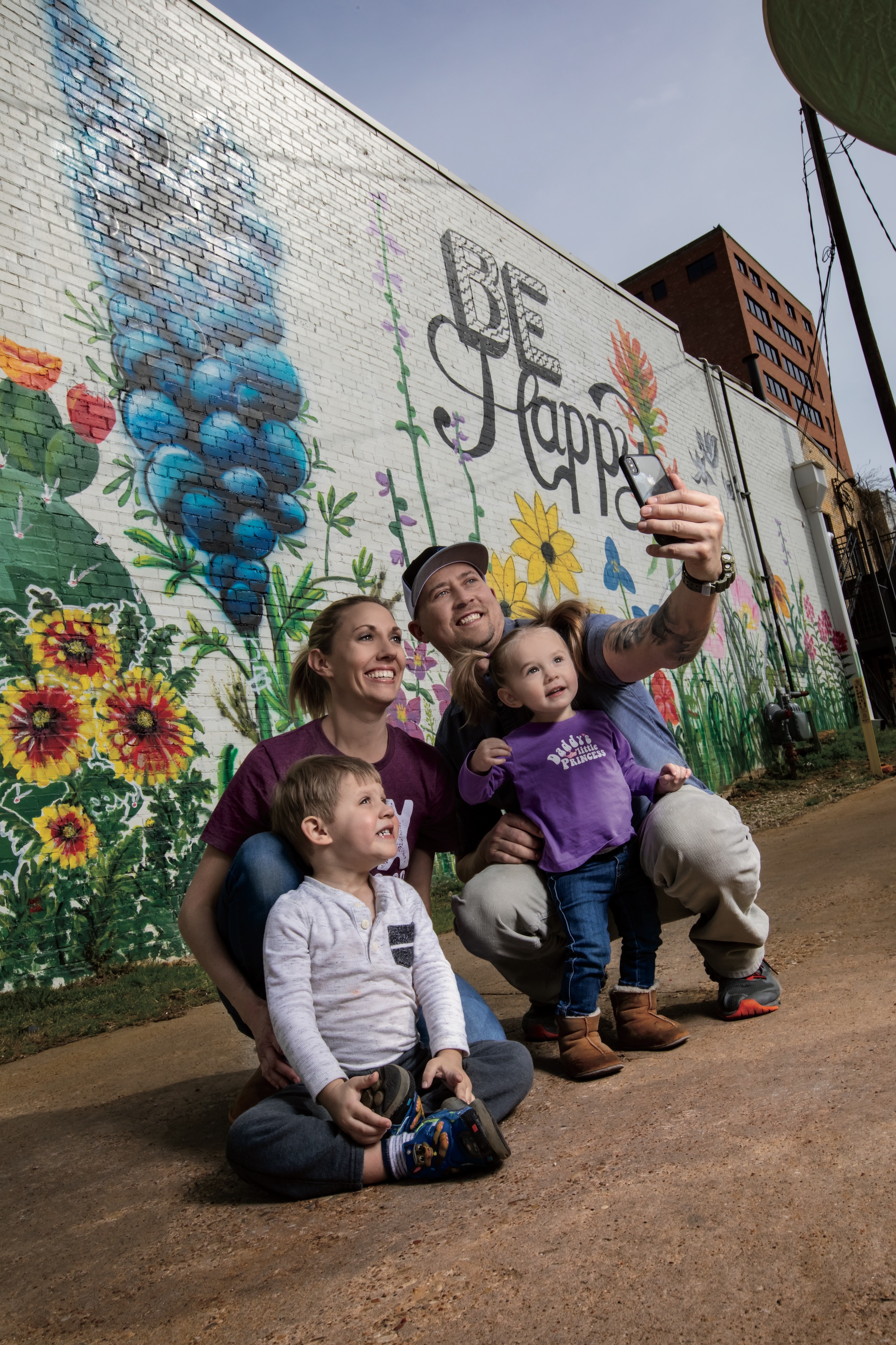 family taking a photo in front of a mural that reads "be happy"